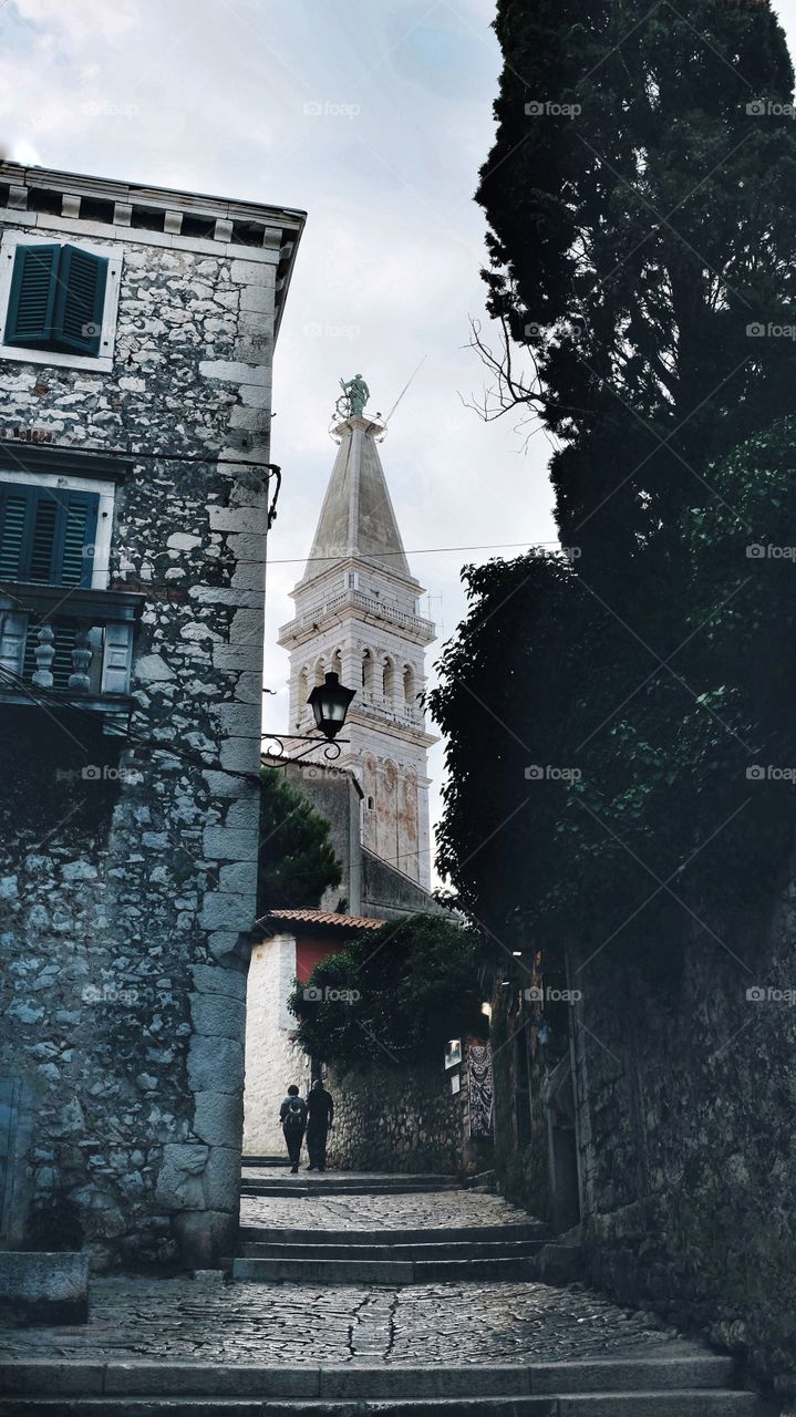 Tourists walk towards the tower of the Church of St Euphemia - as seen from a cobbled street in Rovinj, Croatia.
