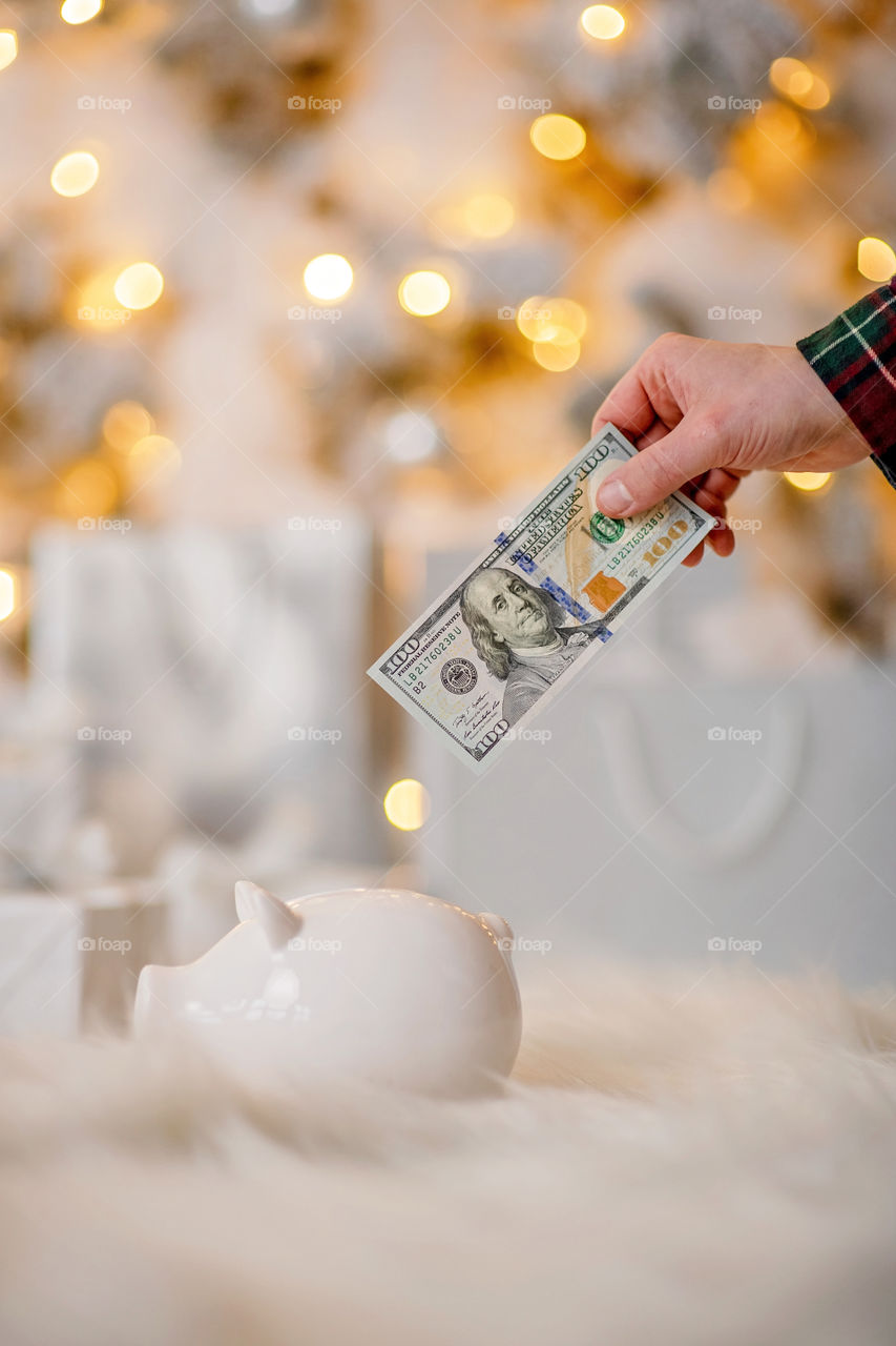piggy bank with 100 dollars banknote in festive New Year atmosphere of scenery. Magical bokeh with Christmas tree and bright lights.
