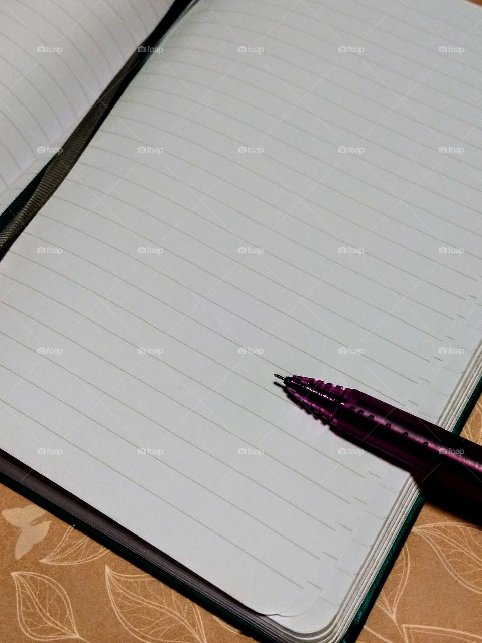 purple pen ready to write in bookmarked journal on pink patterned background