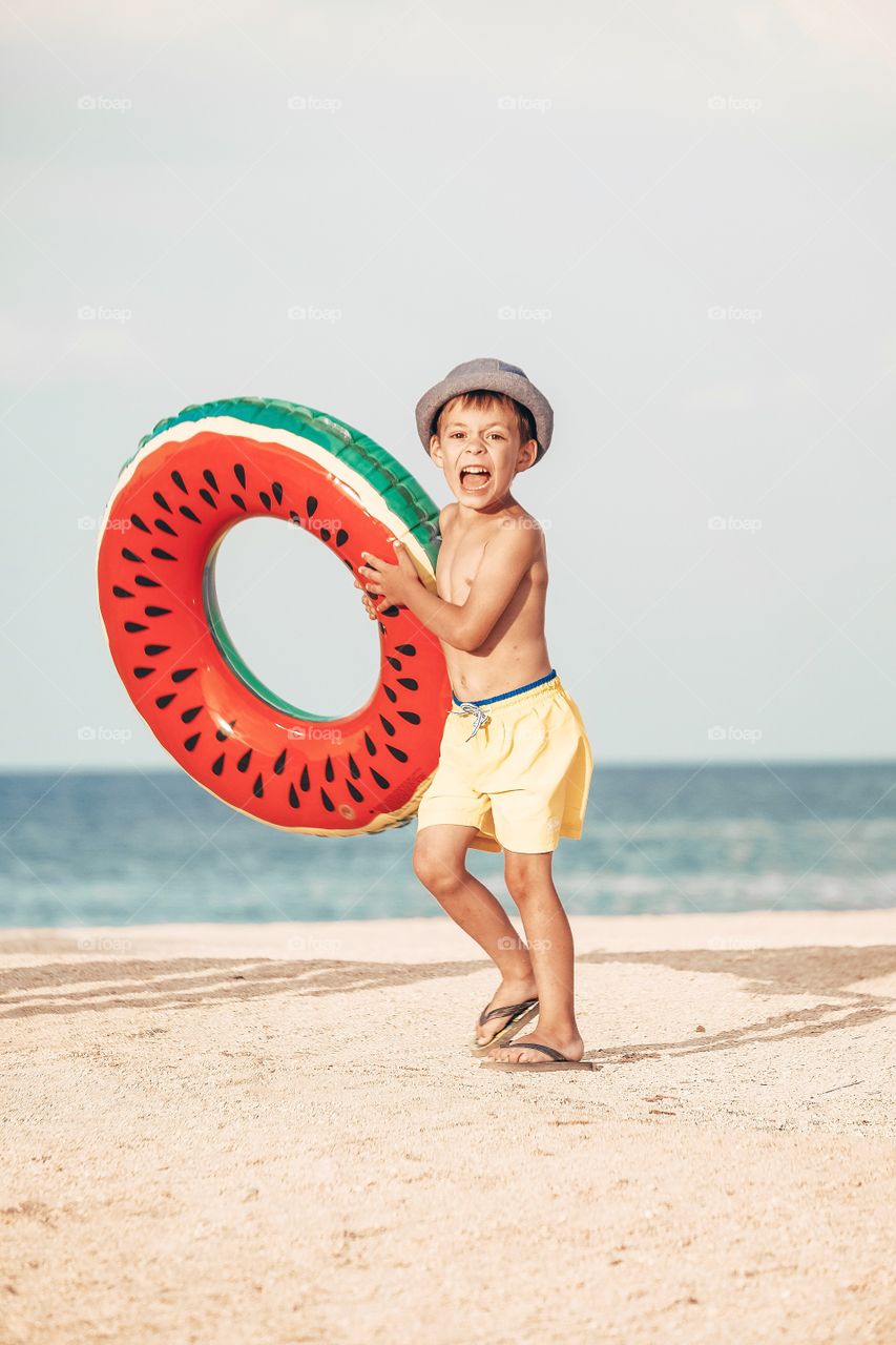 A little boy with watermelon swimming circle at the beach