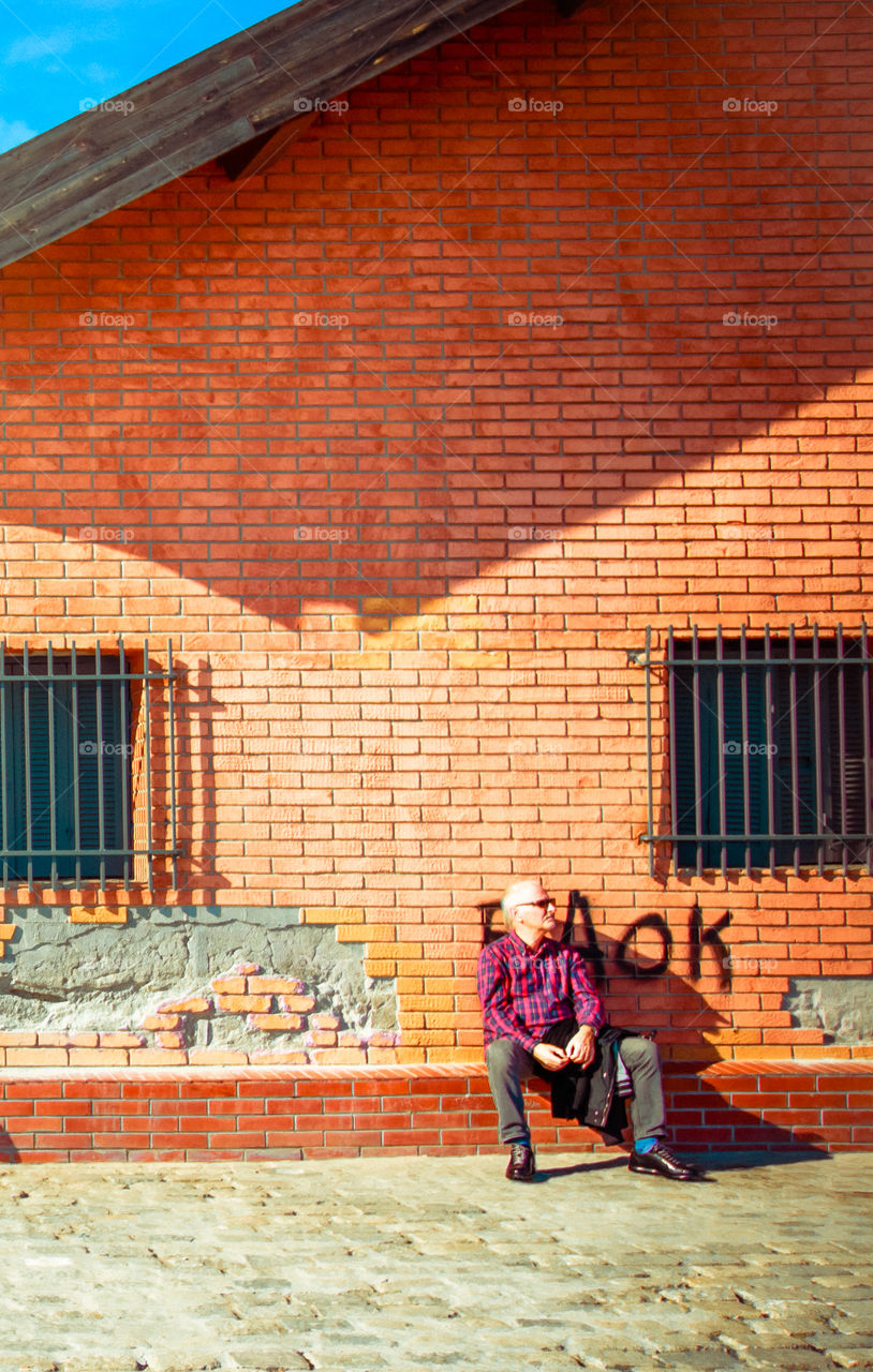 Man Sitting Outdoors In Front Of An Orange Building
