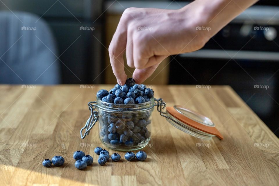 Hand takes blueberry from the glass jar 
