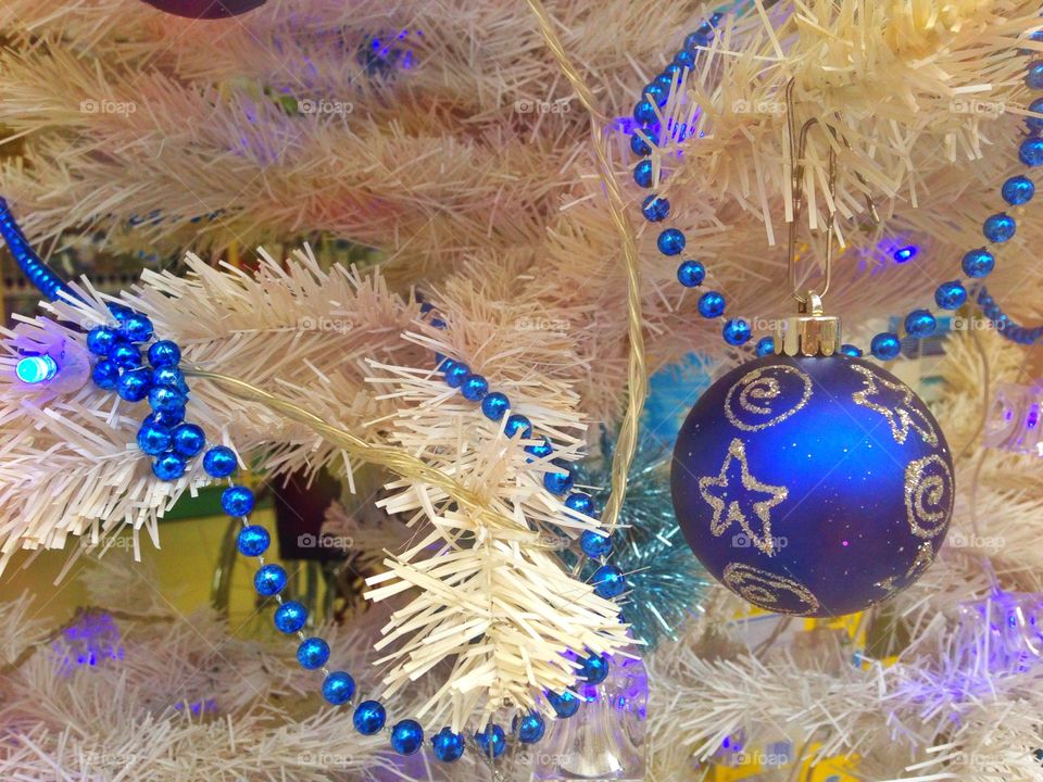 Blue Christmas glass ball and blue bead on white fir tree on colored background 