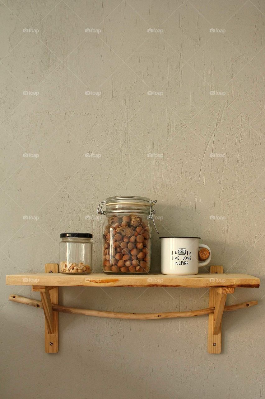 Wooden shelf with glass jars with peanuts and hazelnuts and a tin mug in the kitchen