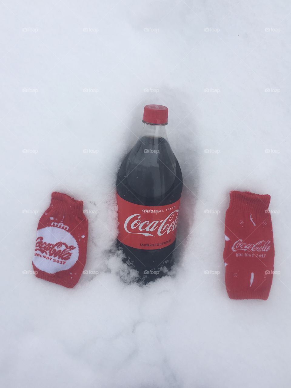 A classic bottle of coke and two coke can sleeves sitting in the freshly fallen cold snow 