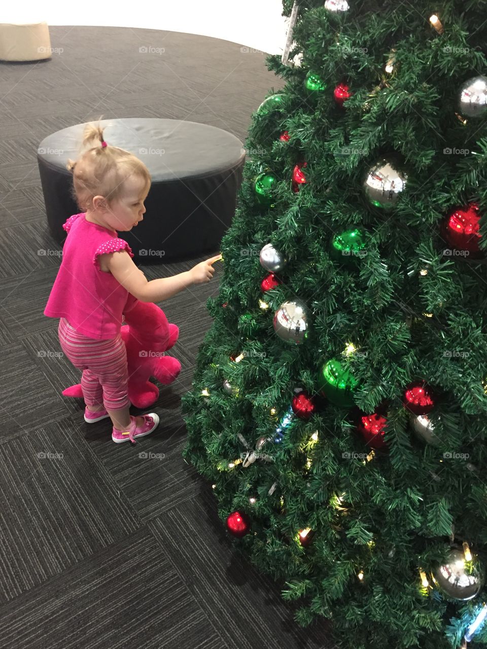 Cute girl with teddy bear standing near christmas tree