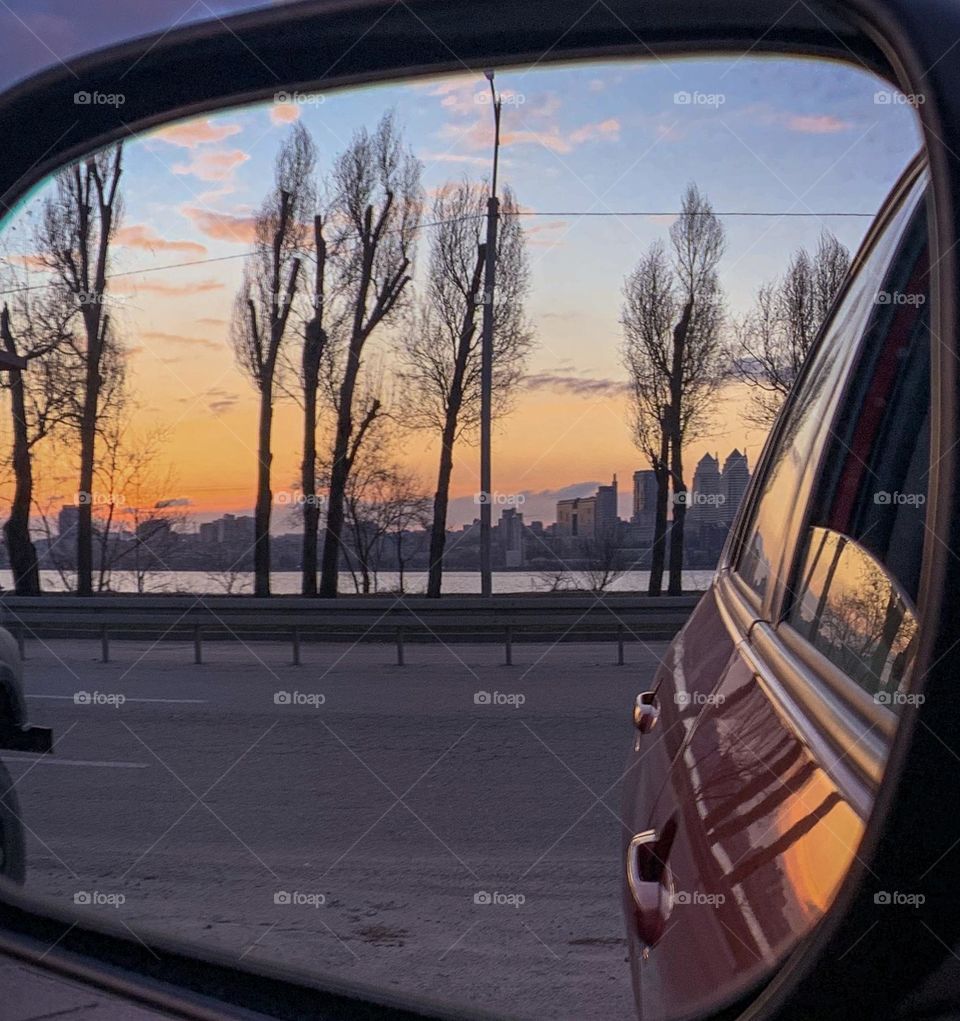 Reflection of sunset sky and cityscape on car’s mirror 