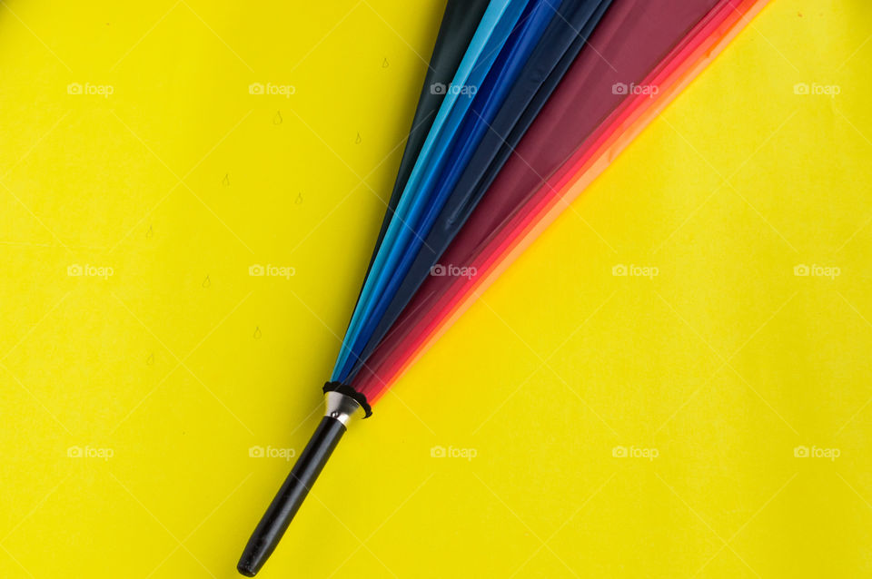 Rainbow colored umbrella on beautiful yellow background.