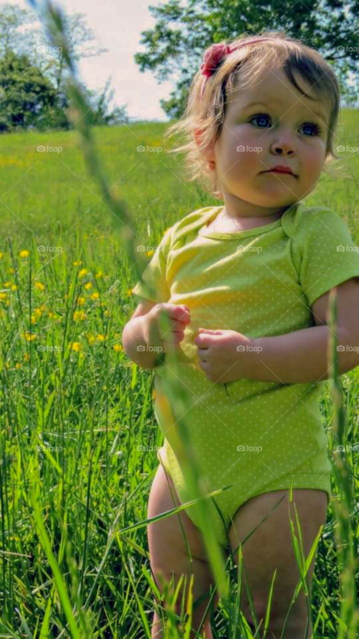 Little girl wearing a onesie standing in a field looking off into the distance.
