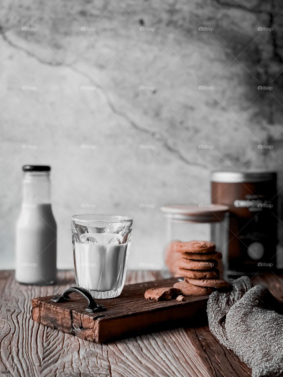 A cup of milk and stacks of biscuits with blurry milk bottle and biscuits jar as background 