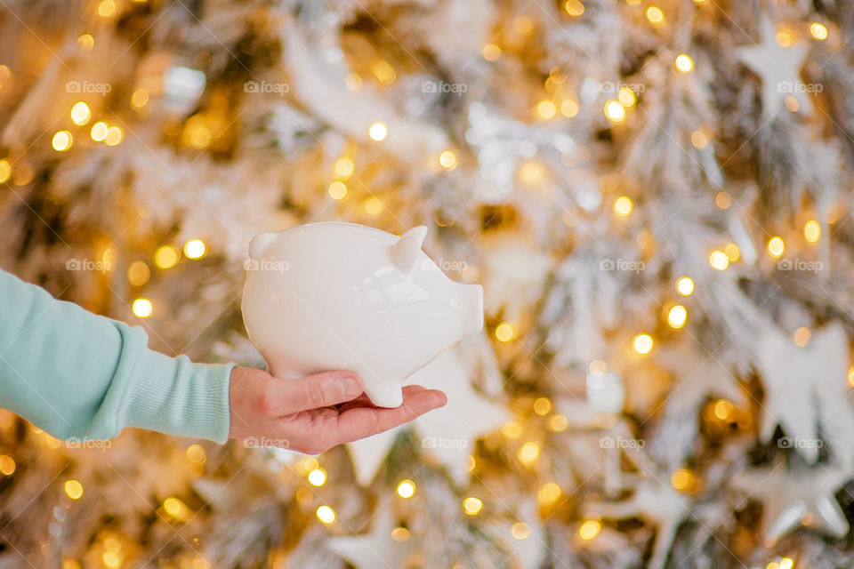 piggy bank with 100 dollars banknote in festive New Year atmosphere of scenery. Magical bokeh with Christmas tree and bright lights.