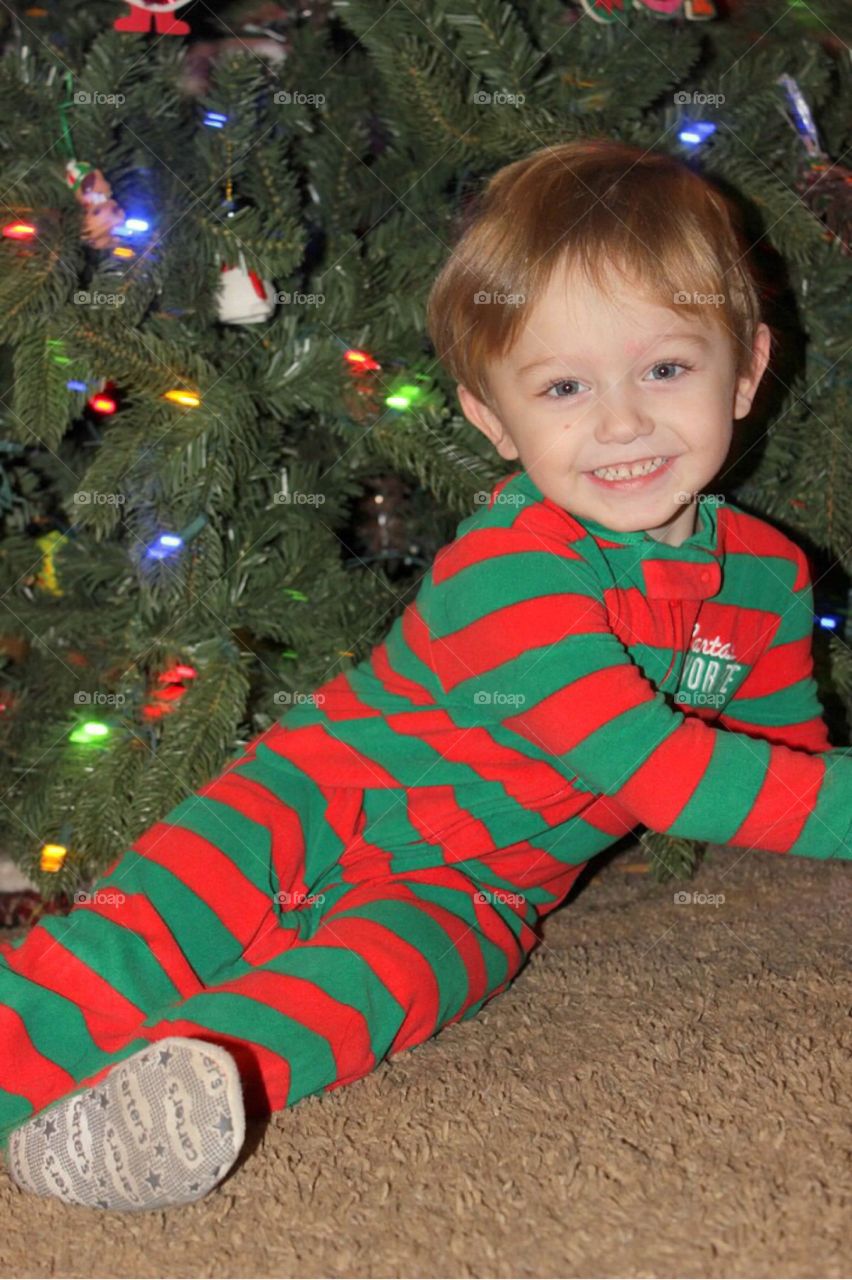 A little boy smiling in front of Christmas tree