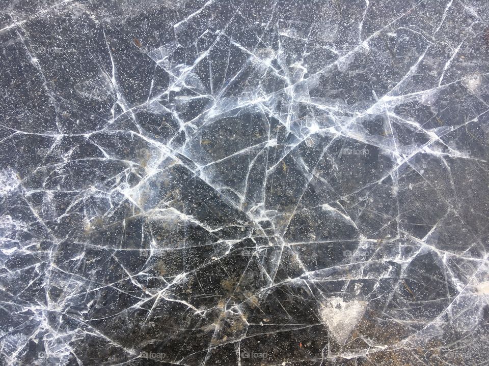 Cracked ice over a puddle off Cross Keys Roundabout, Gloucester. A small heart is visible to the bottom right hand side. Noticed on a Winter walk.