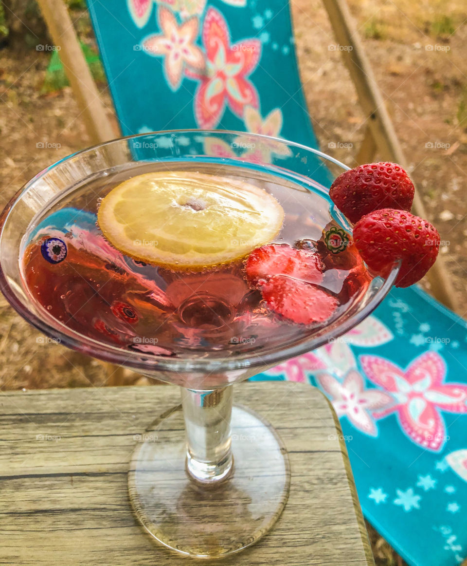 A cocktail with lemon and strawberries sits ready to be drunk next to a colourful deckchair