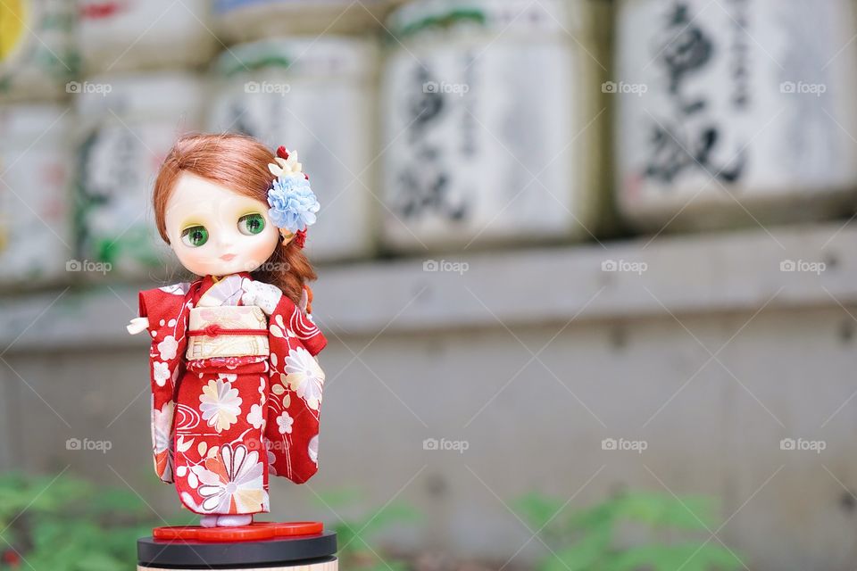 Cute doll in Kimono. A cute doll is dressing up in a red kimono. Kimono is a traditional Japanese garment. The doll is standing in Front of Japanese sake barrels. 