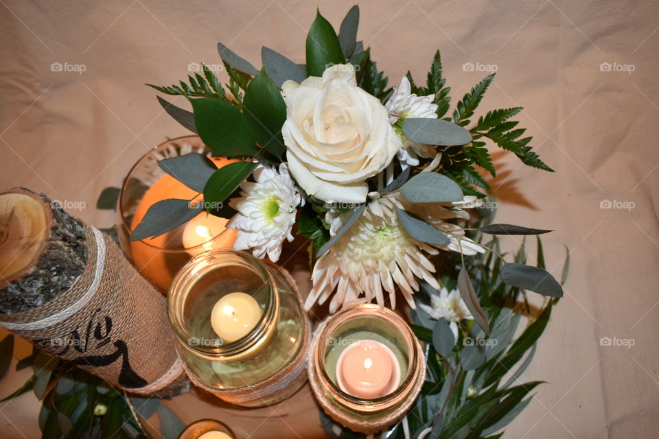 Surrounded by gold accented candle light a bouquet of greens and flowers in shades of white create a whimsical and rustic centre piece. The willow at the base grounds the arrangement. 