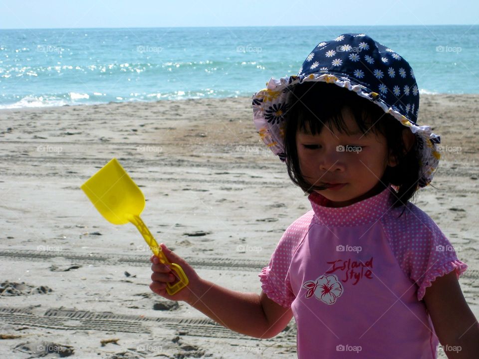 Cute little girl in pink w hat at the beach with sand scooper