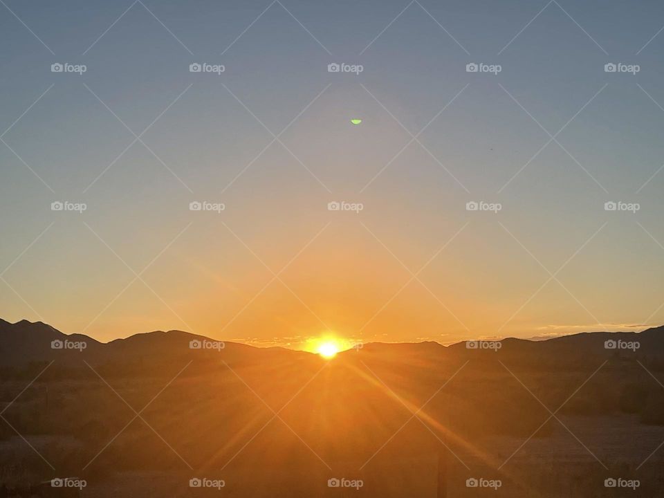 A orange sunset with mountains and the sun peeking over the mountains.