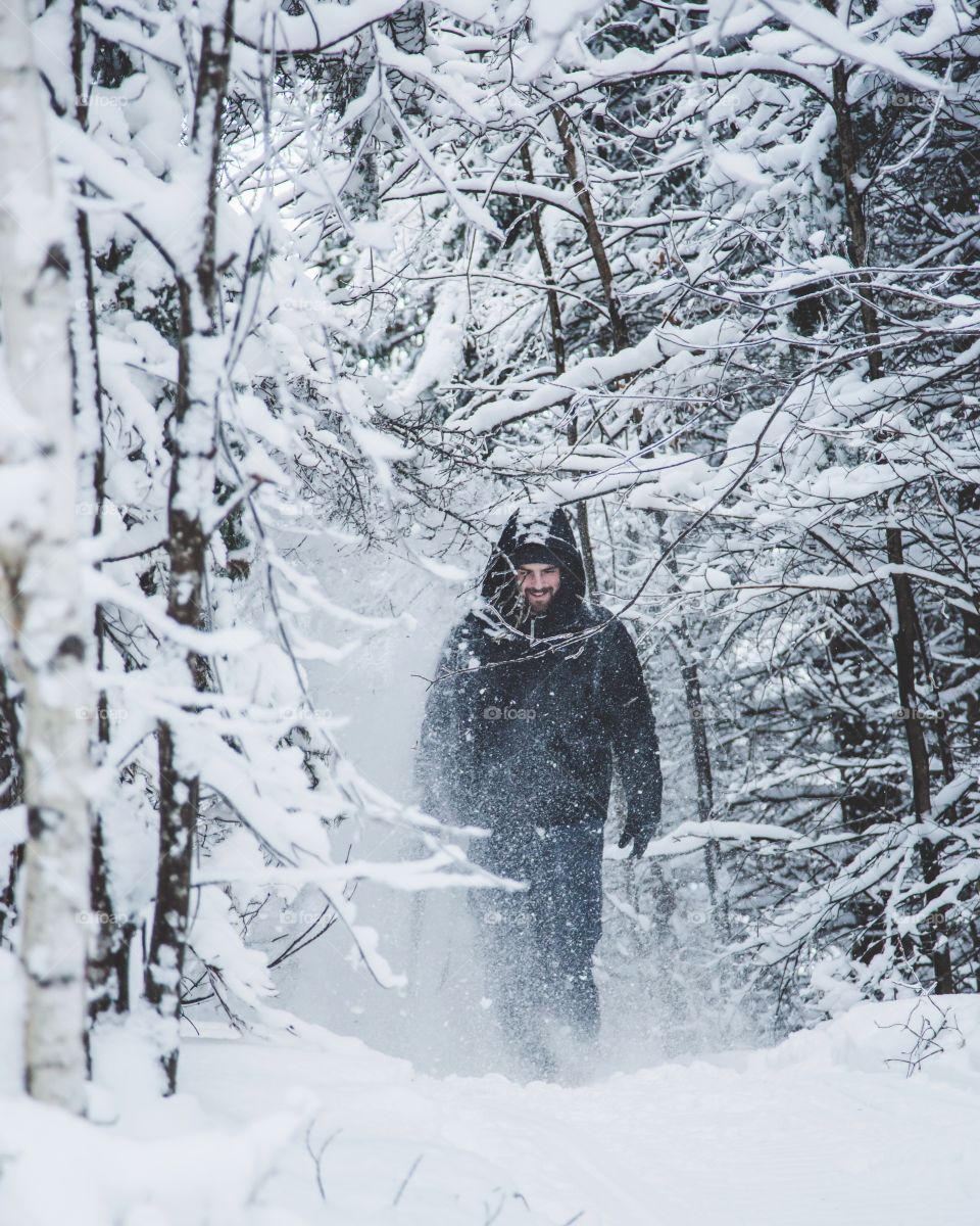 A young man hiking through a massive snowy forest, exploring and covered in snow