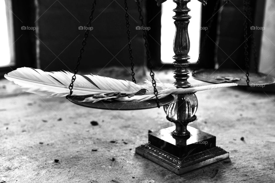 Black and white image of a feather and small stones on a balance scale