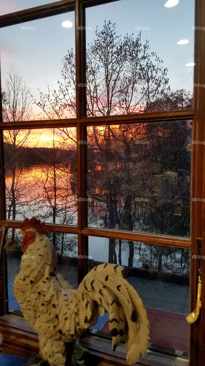 a wooden rooster in the kitchen looking at the sun setting