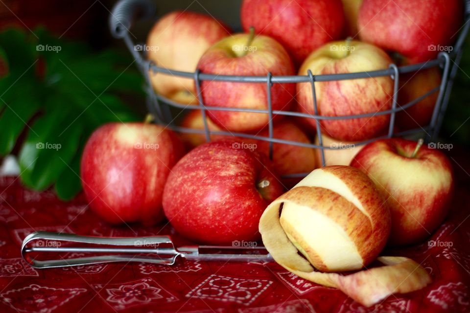 Fruits - Gala apples in a wire basket with a partially peeled apple and peeler on a red bandana-print tablecloth