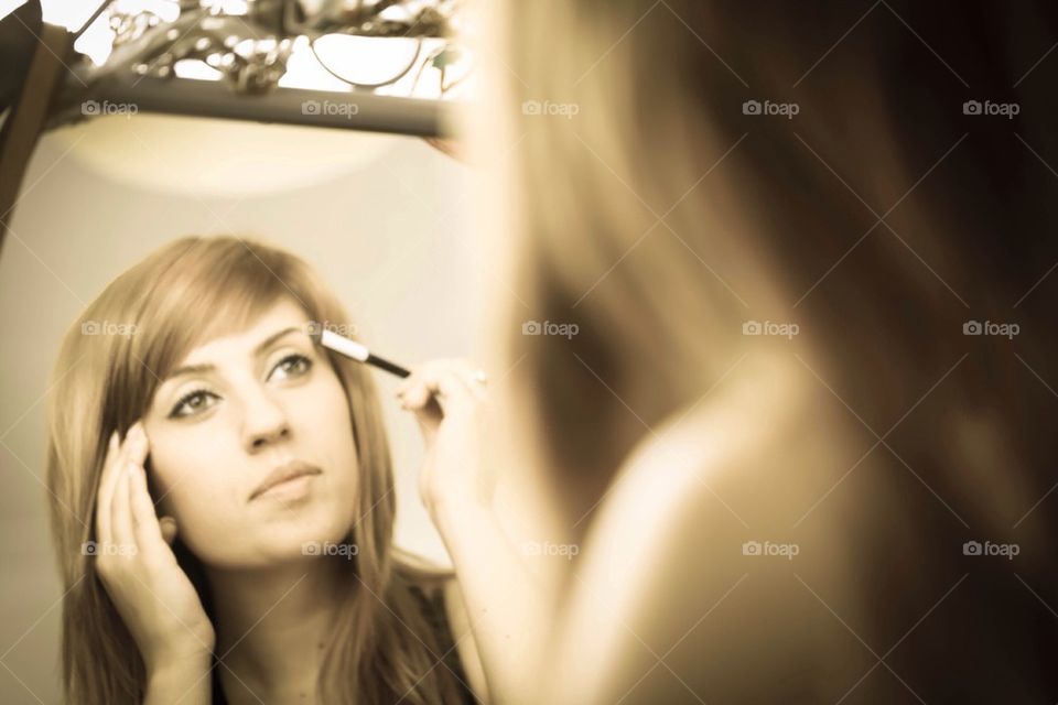 Girl applying make -up and her reflection in the mirror 