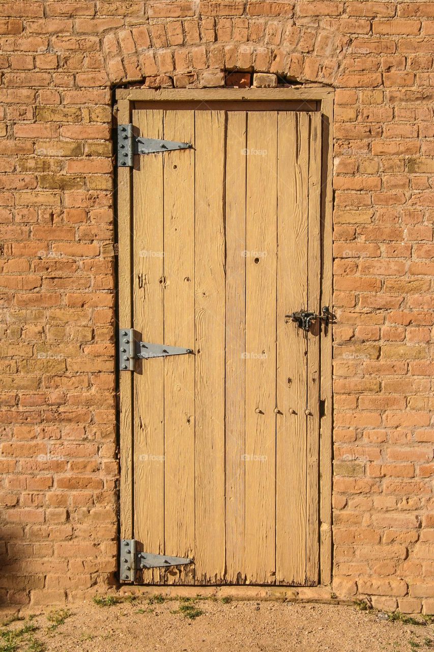 Old wooden door of an old brick building harkens a vibe of the old west, semi monochromatic with vintage hardware 