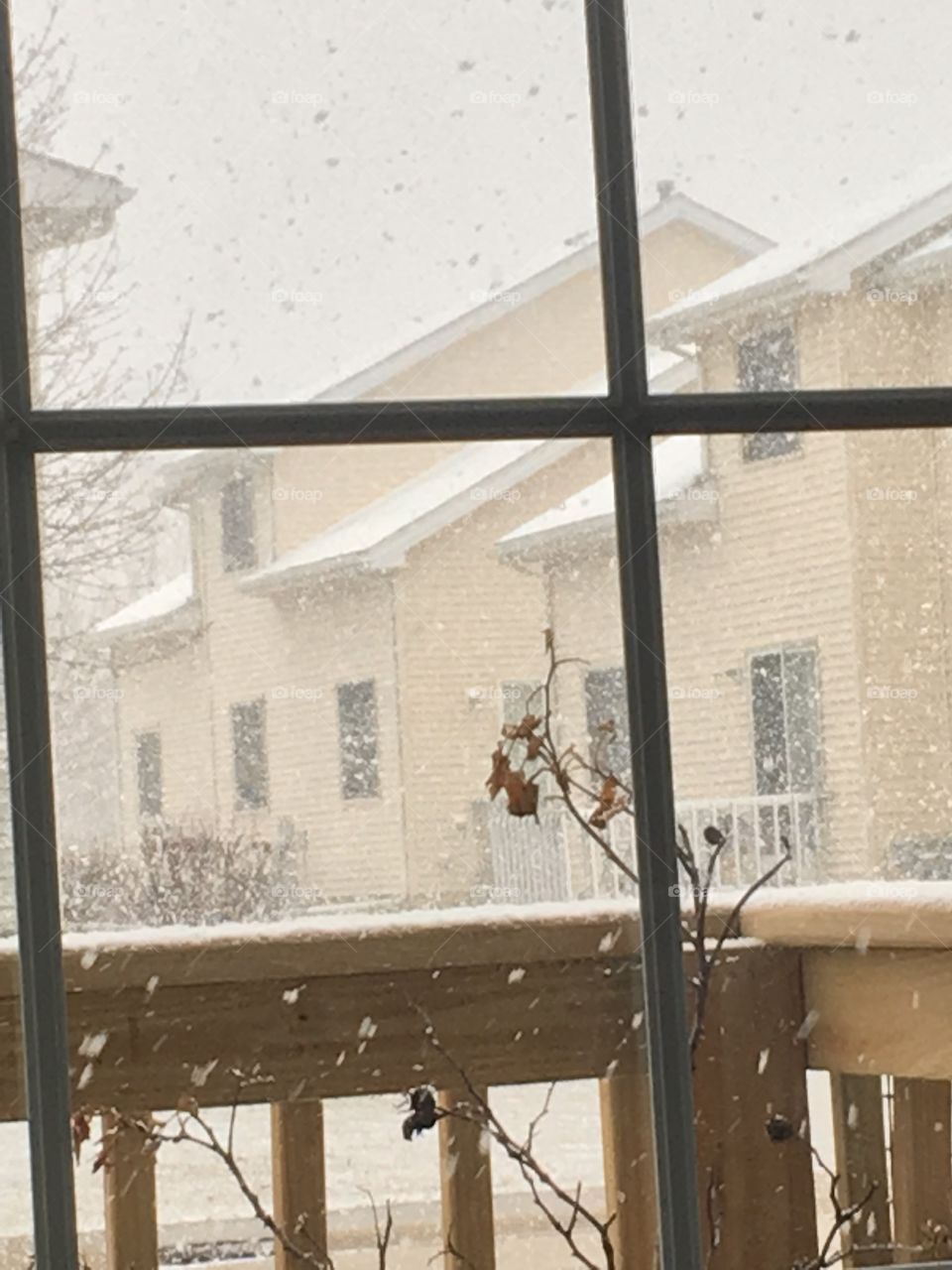 Raining snowflakes through sliding glass window pane against yellow apartments architecture in winter