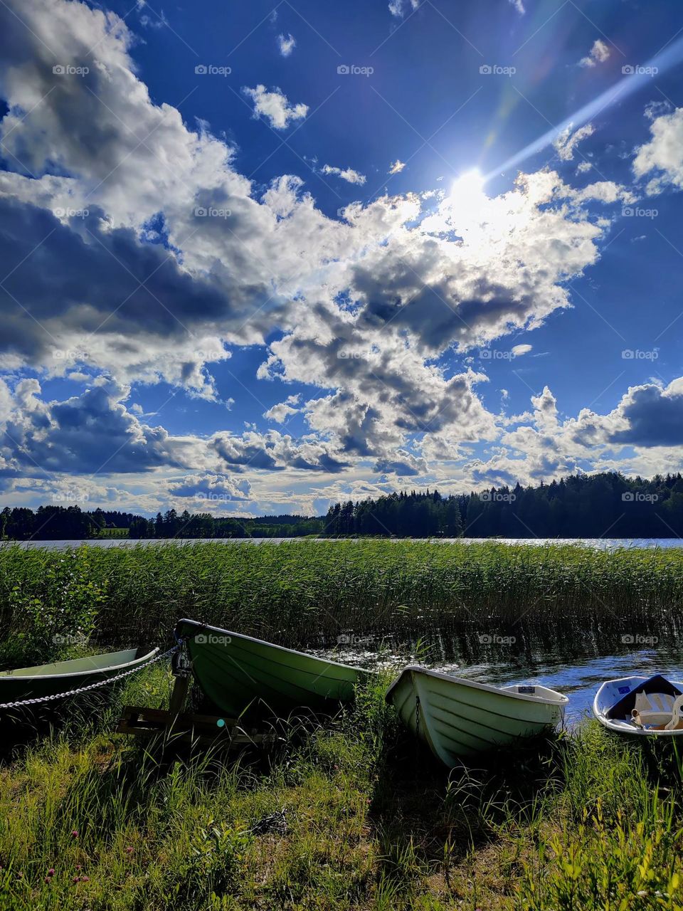 Beautiful landscape with the sun shining through the clouds over the lake shore with boats, reeds and tree-line on the horizon 