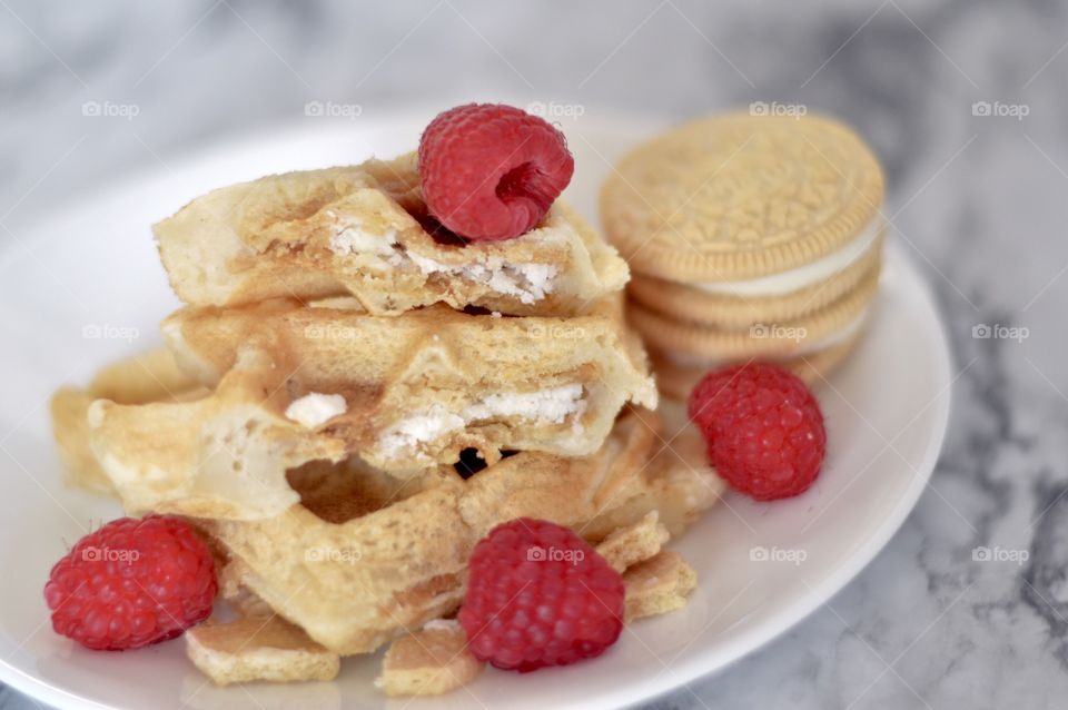 Golden double stuff Oreo cookie waffle and raspberries on a white plate