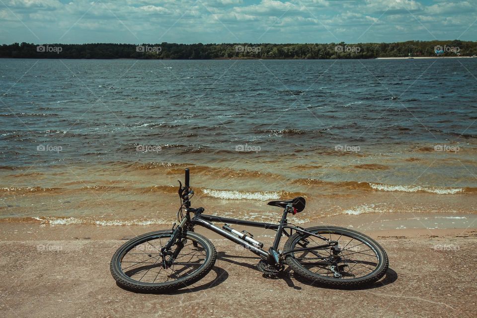 A deserted bicycle rests on the serene banks of a river, hinting at a story of solitude and quiet reflection