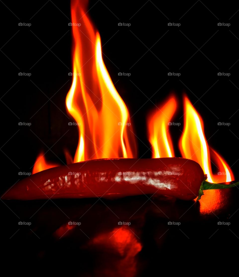 Chili pepper in flame of fire on black background