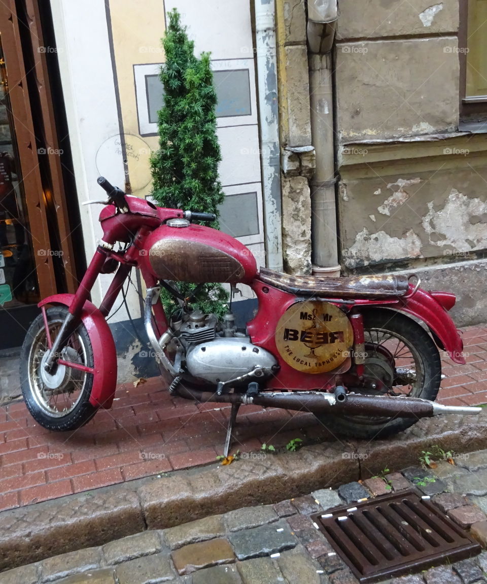 Old rusty metal burgundy bike motorcycle with beer bar advertising banner parked on the side road