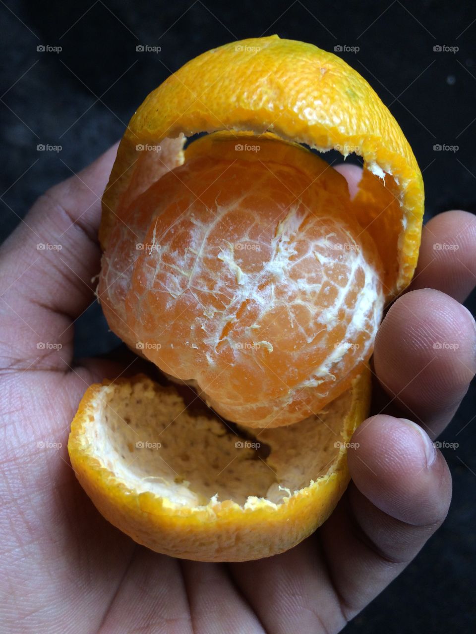 Directly above of hand holding orange fruit with peel