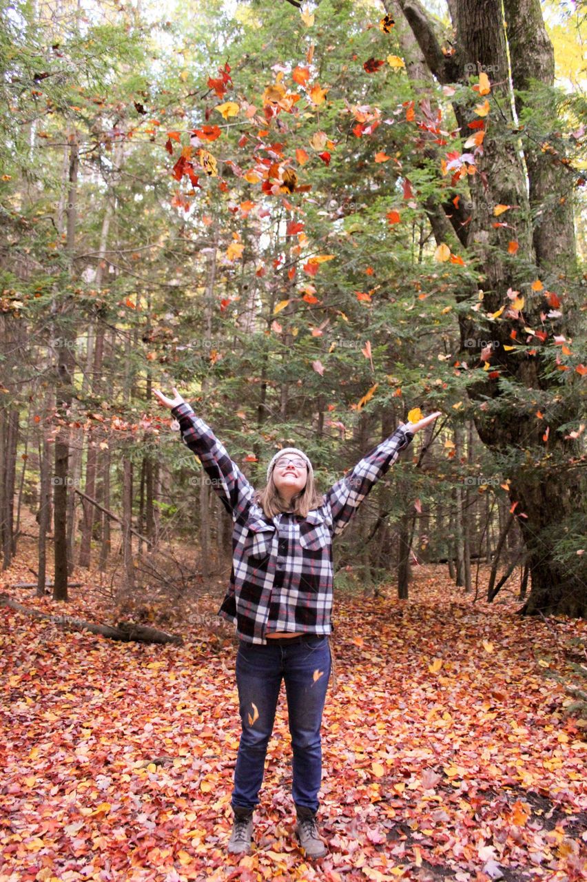 Young woman playing with leaves in the woods in the fall