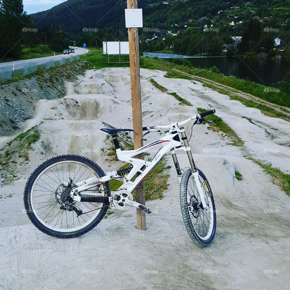 Picture of a white downhill bike in front of a bicycle jumping park
