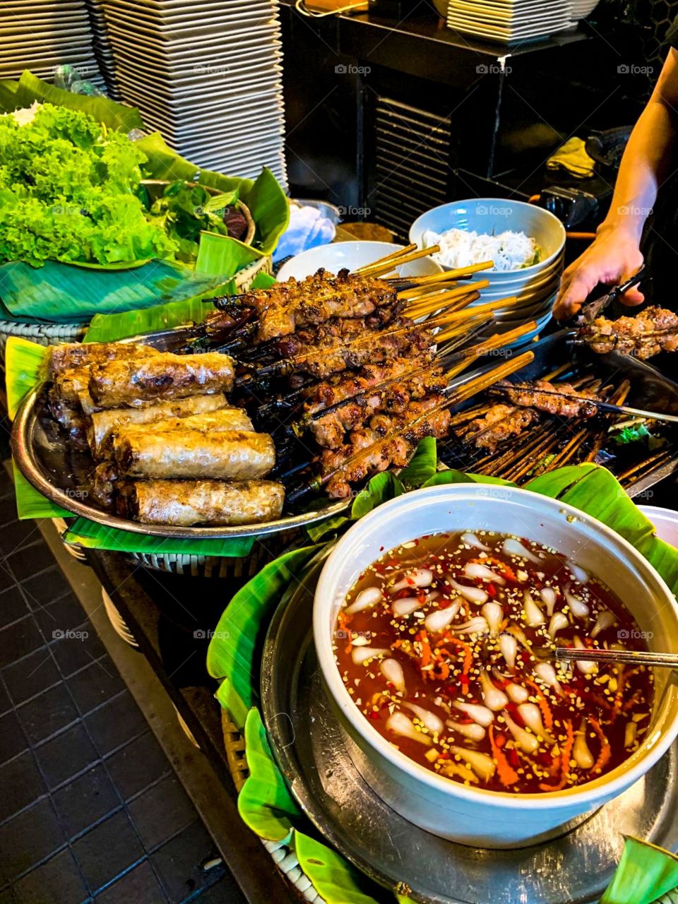 grilled meat spring rolls noodle dishes on the table.with delicious grilled meat skewers, crispy spring rolls, white noodles , green salads and a bowl of chili garlic fish sauce. This food is very delicious