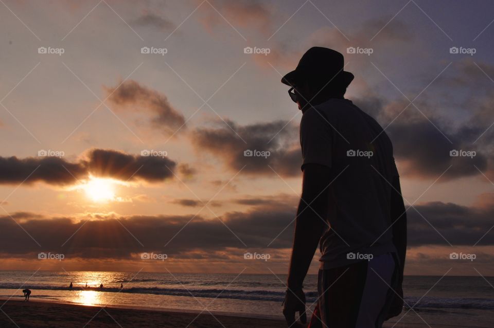 Young man walking in the beach at sunset