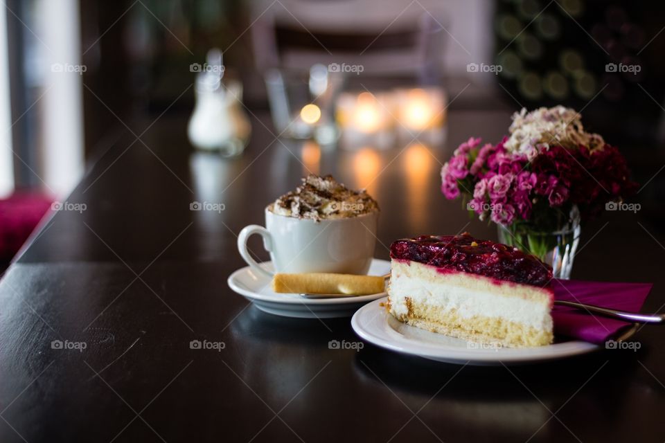 Piece of fruit cream cake with a cup of cappuccino on café table