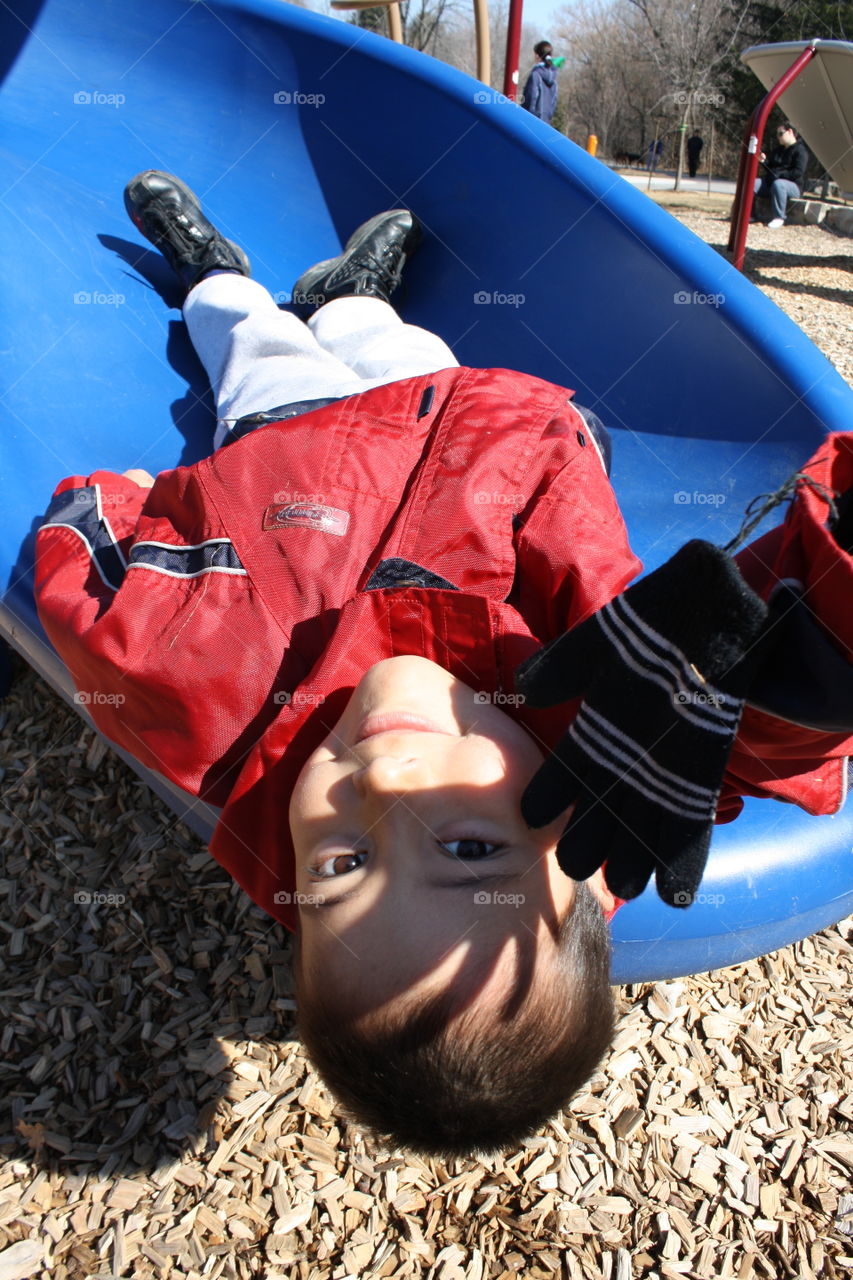 Cute boy laying up side down on a slide