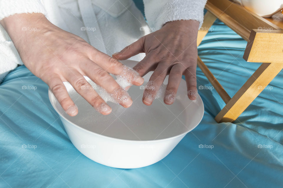 A man at home takes care of himself and does a manicure at home on a blue background and with orange.
