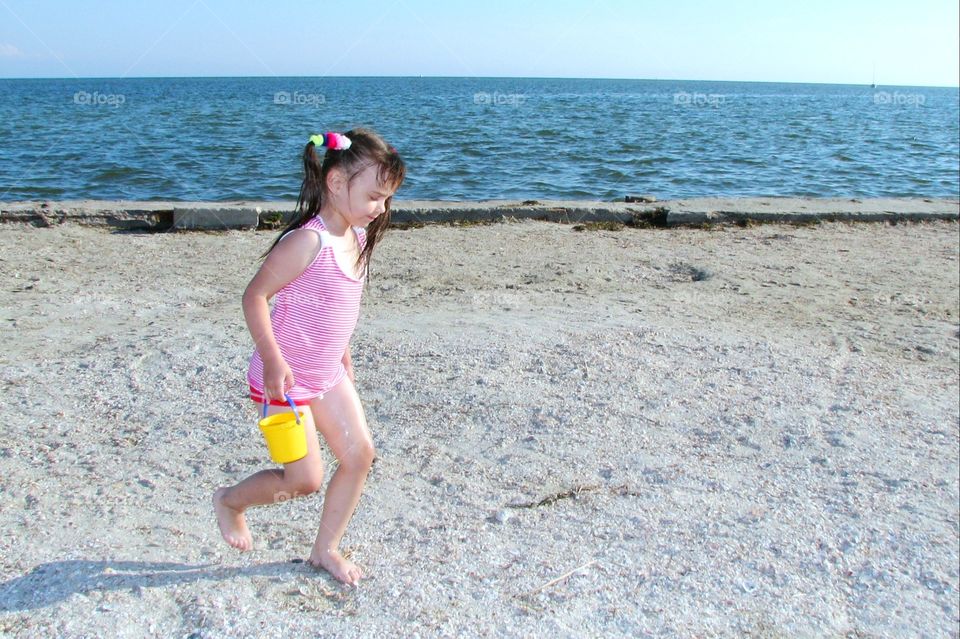 girl walking on the sand with a bucket