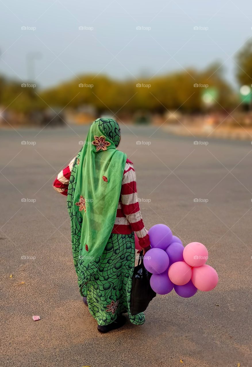 indian woman in saree holding colourful purple and pink balloons