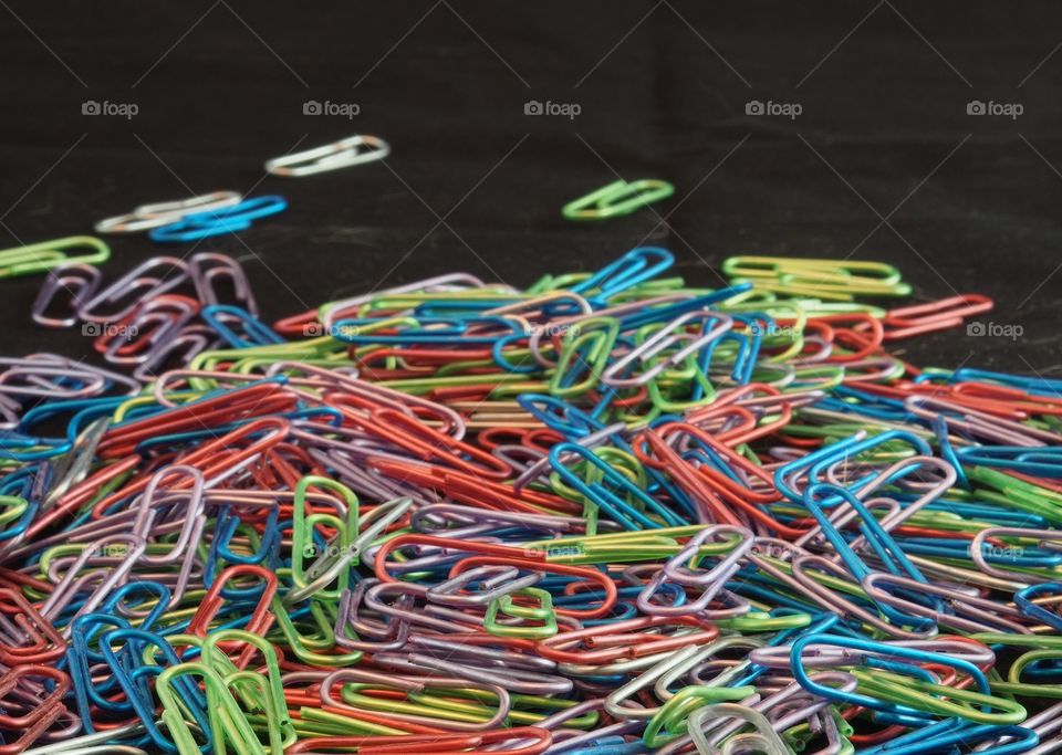 A pile of paper clips of many different colors against a black background. 
