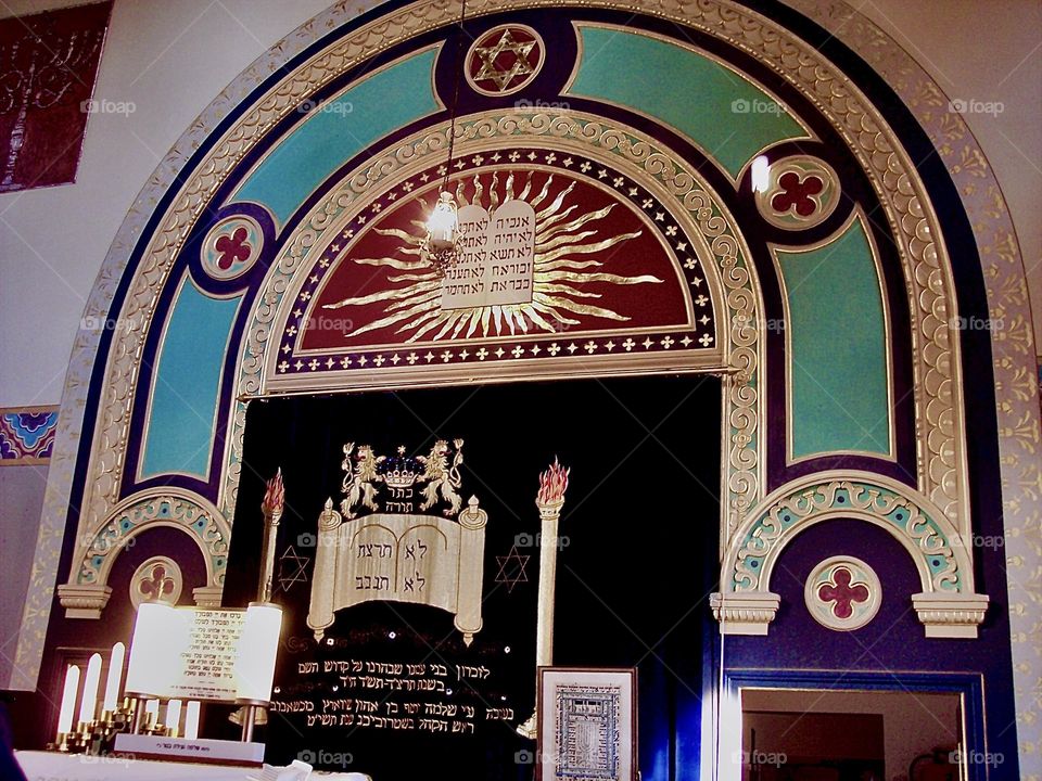Above the large arch inside the synagogue is a golden plaque inscribed in flaming Hebraic letters, a rendition of the “Torah”, the book inspired by the Judaic/Christian God JHVH a.k.a. the Old Testament. 2020. Hypnotic Productions