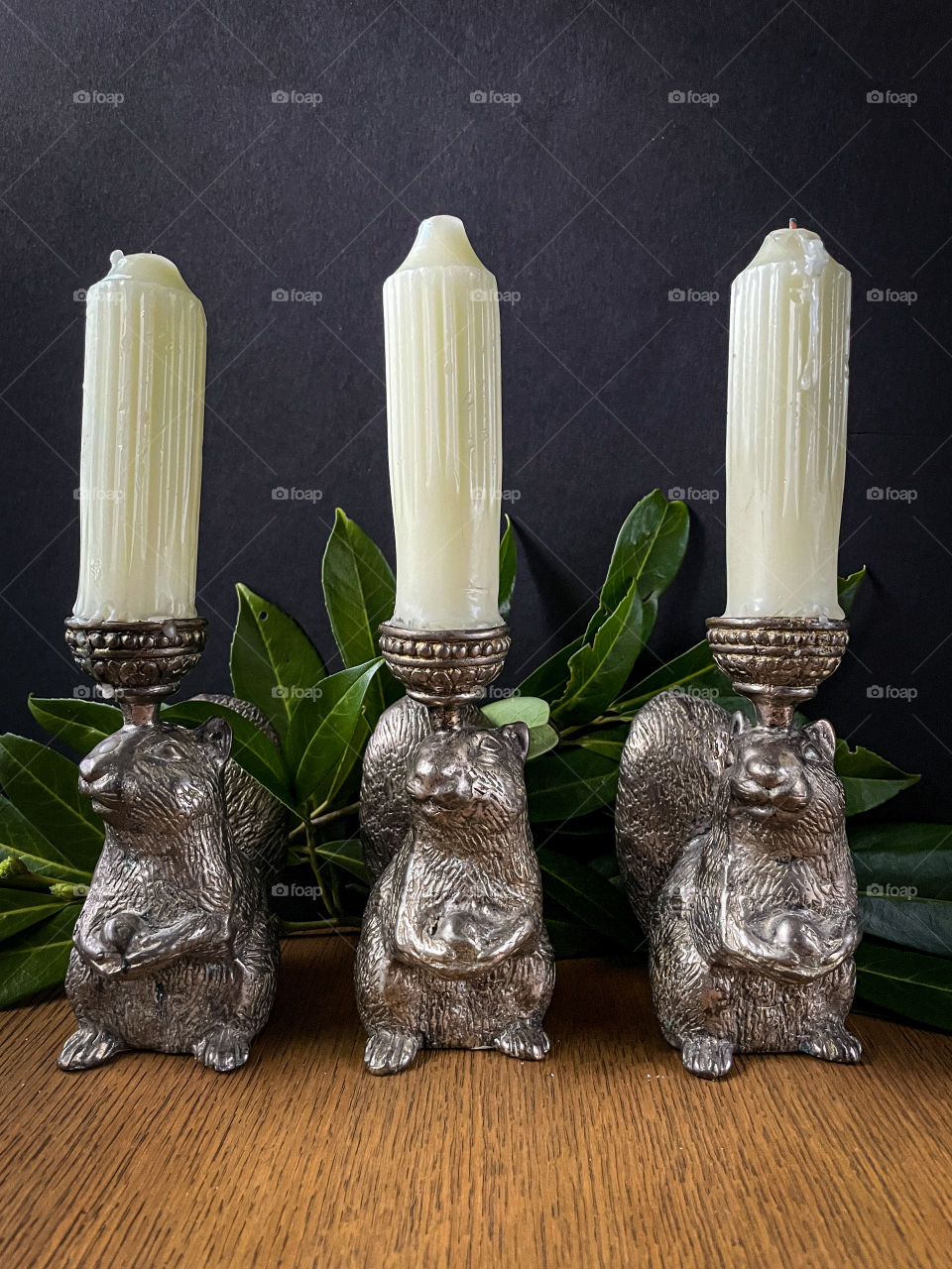Three squirrel candle holders from Arhaus supporting cream candles with a splash of greenery. 