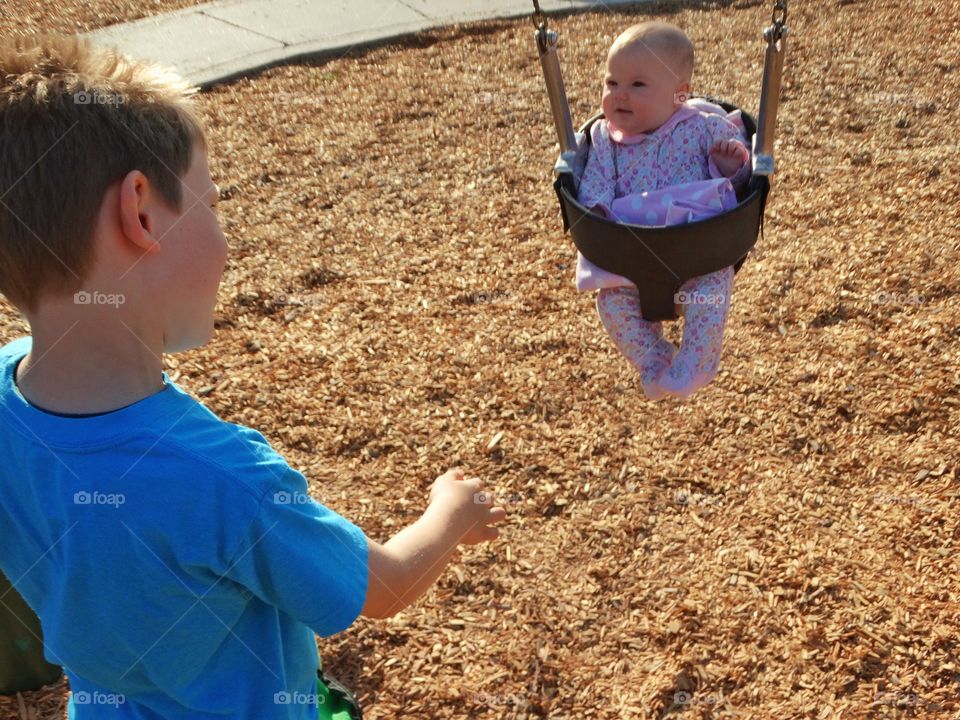 Boy Pushing Baby In A Swing
