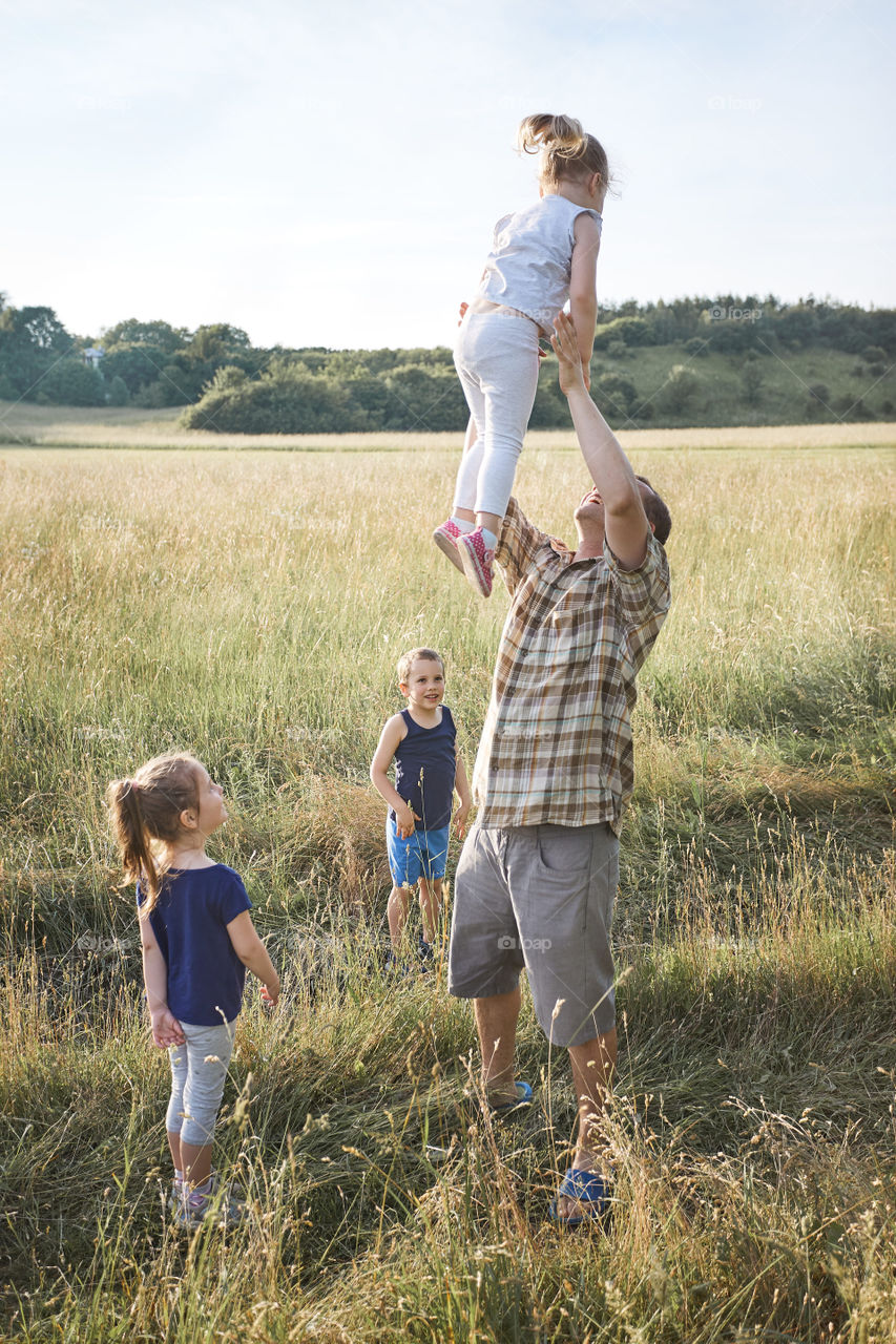 Father tossing little girl in the air. Family spending time together on a meadow, close to nature. Parents and children playing together. Candid people, real moments, authentic situations