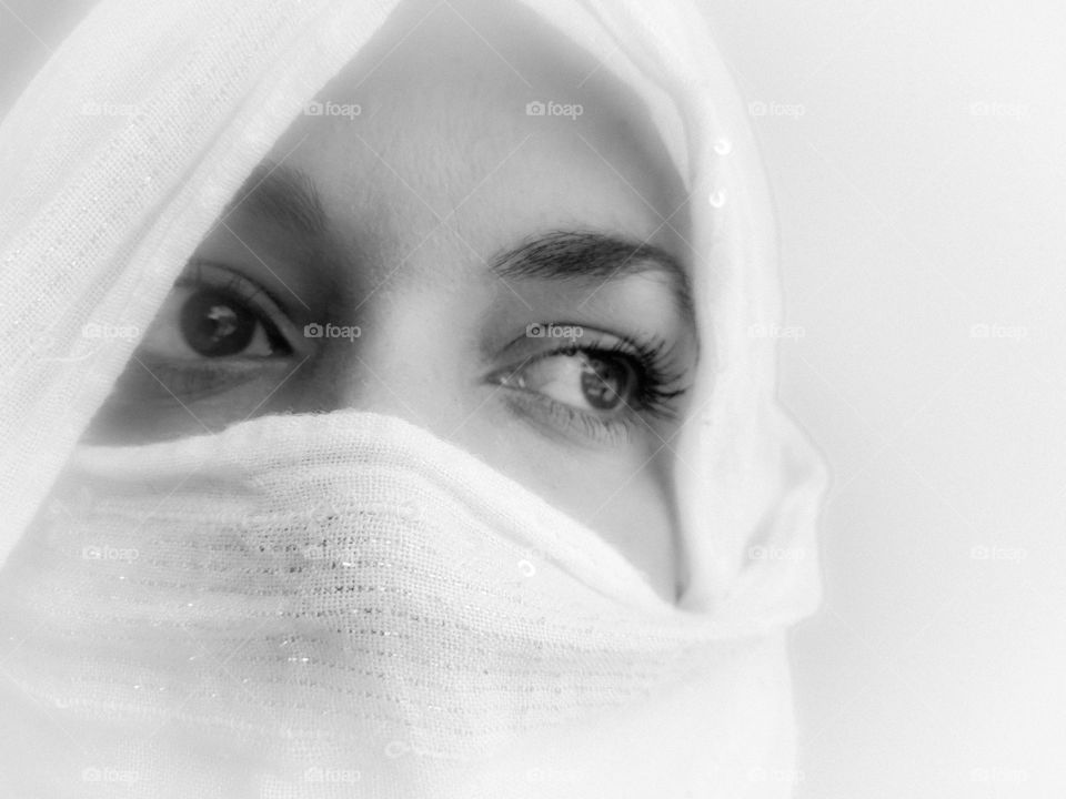 Black and white portrait of a woman covered in a white scarf during the pandemic, looking away in concern. White background.